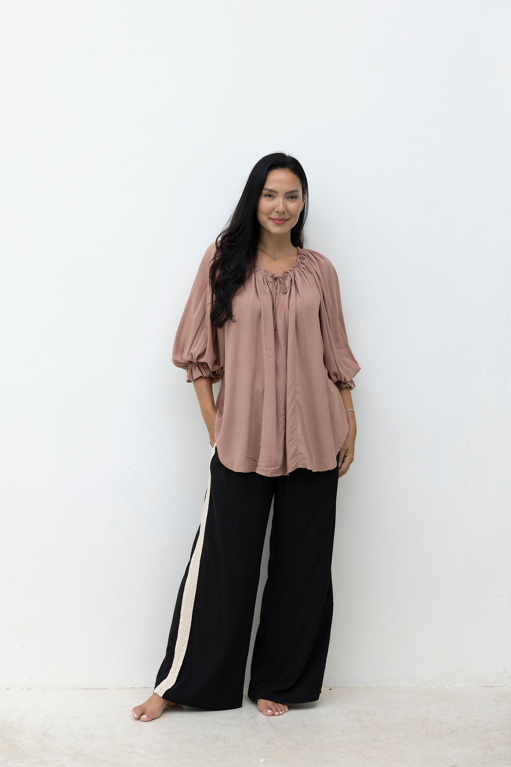 Woman wearing a brown blouse and black pants with white stripes on a white background