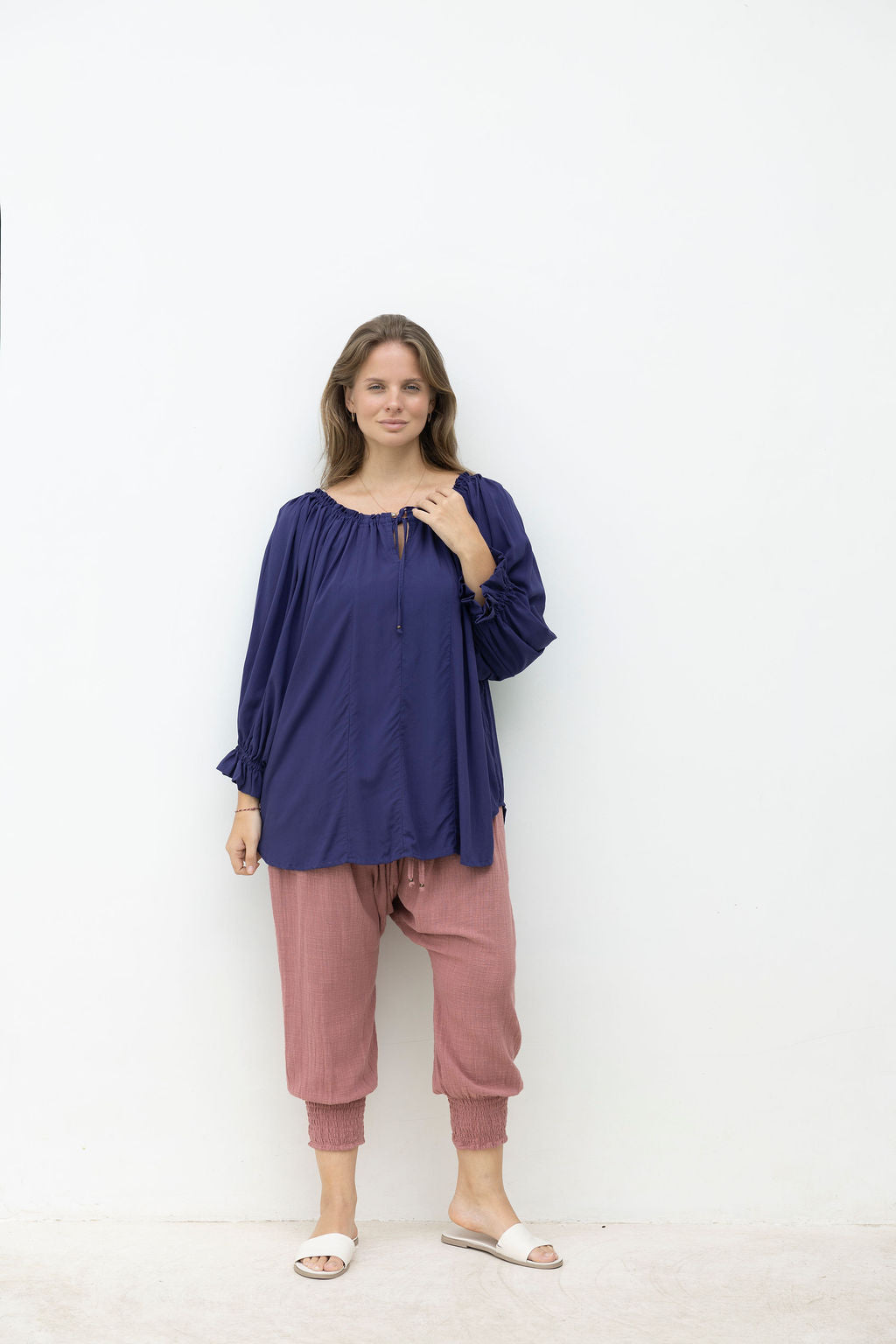 Woman wearing a blue top and pink pants against a white background