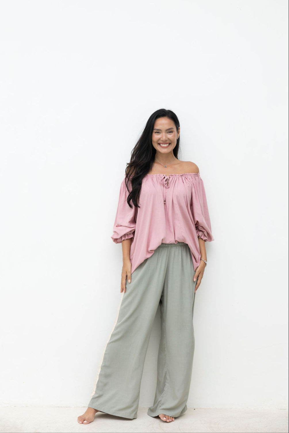 Woman wearing a pink off-shoulder top and gray wide-leg pants on a white background