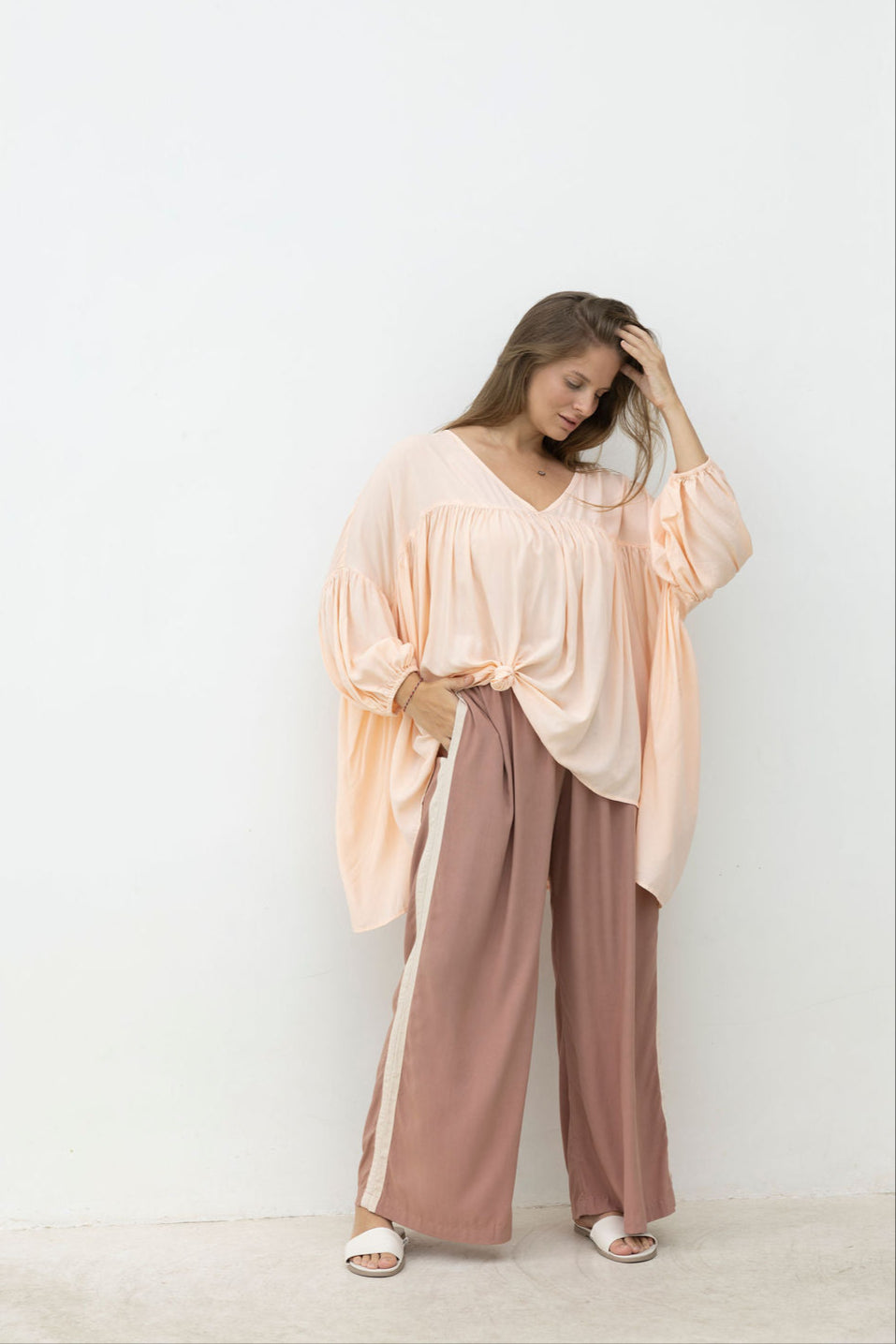 Woman wearing a light pink top and brown pants against a white background