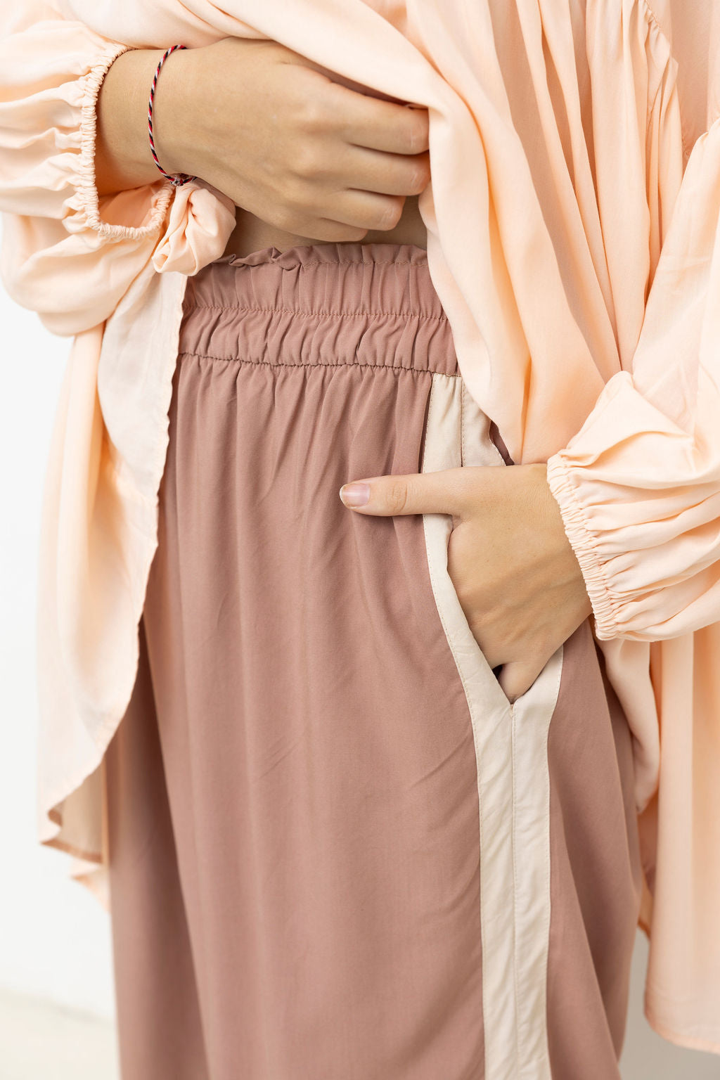 Person wearing a pink top and brown pants on a light background