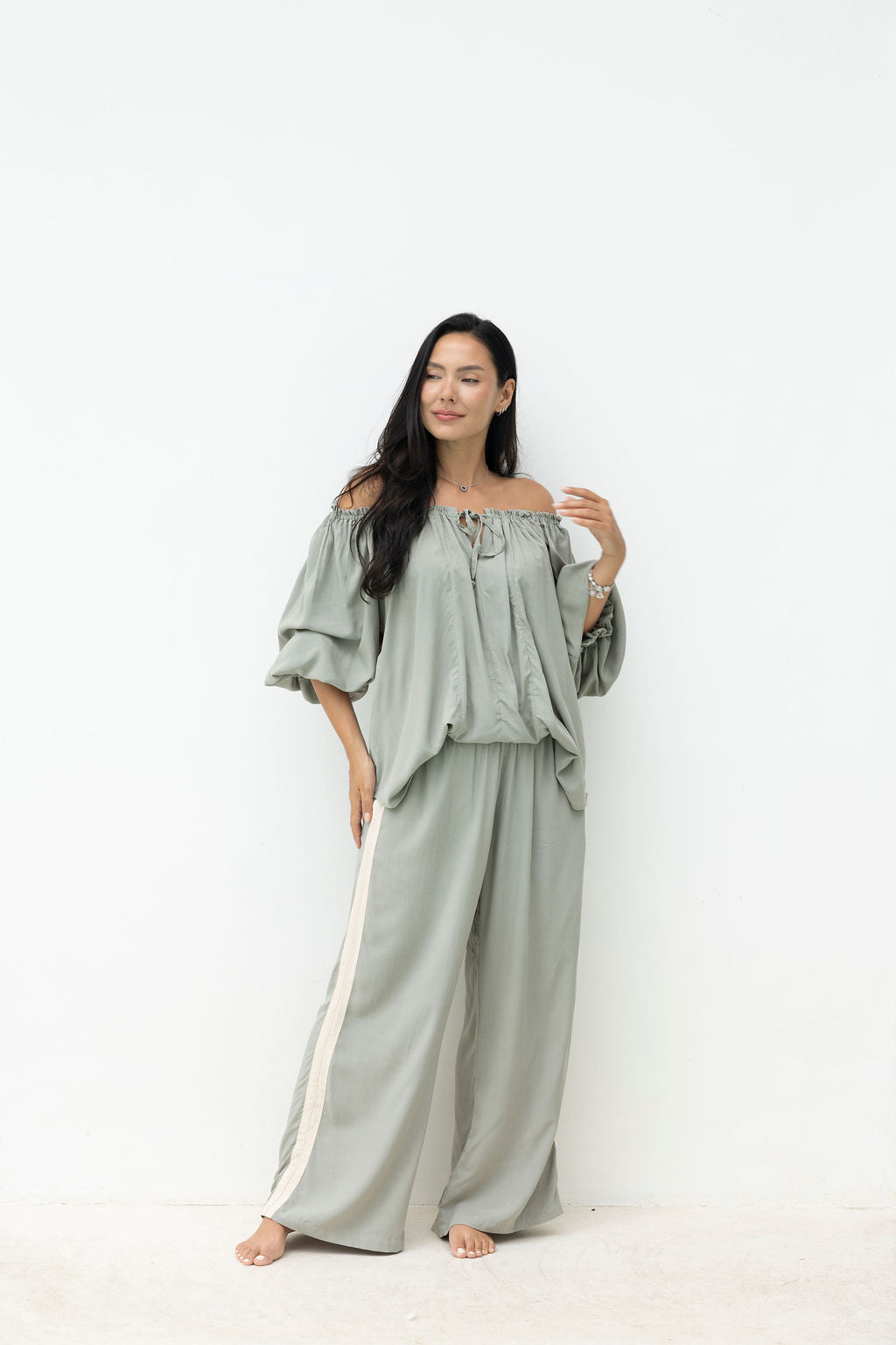 Woman wearing a light green off-shoulder top and wide-leg pants on a white background