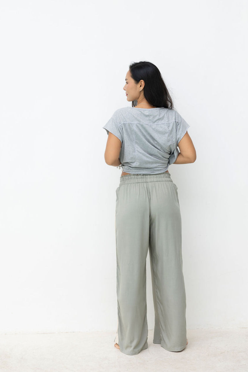 Woman wearing a light gray t-shirt and wide-leg pants standing in front of a white wall