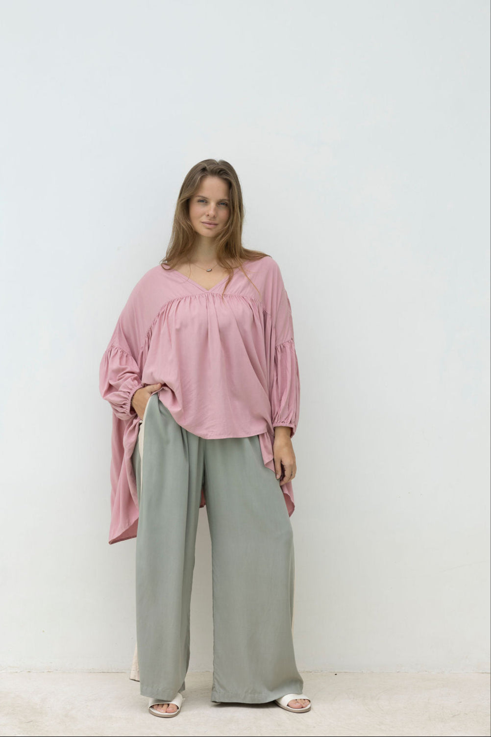 Woman wearing a pink blouse and geen pants against a white background